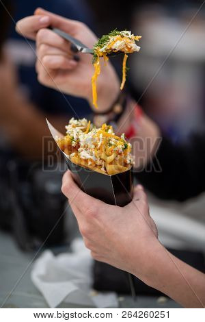 Close Up Of Hands With Fork Picking Up French Fries With Cheddar And Yellow Cheese And Dip. Fast Foo