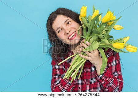 Laughing Young Caucasian Woman With Bouquet Of Tulips On Blue Background.