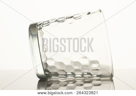 Empty Glass Lying On Reflective Surface. Close Up. Glass Cup On A Reflective Surface Isolated On Whi