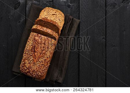 Loaf Of Sliced Whole Wheat Bread On Dark Dishtowel Over Black Wooden Table. Top View With Copy Space