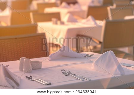 Chairs And Tables At Sunset At Hotel Restaurant. Cutlery And Napkings On Tables.