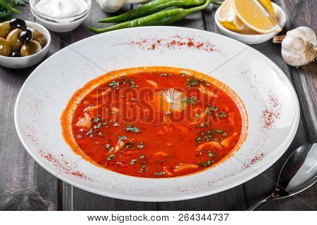 Soup With Meat, Olives, Herbs And Lemon In Plate, Served With Sour Cream, Peppers On Dark Wooden Bac