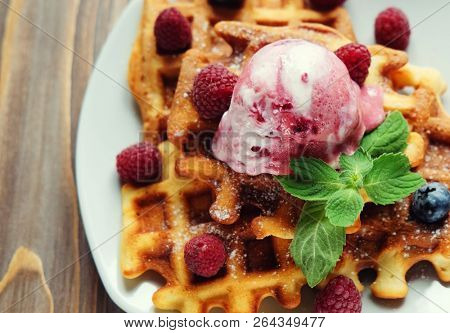 Plate of belgian waffles with ice cream and fresh berries - raspberries and blueberries.