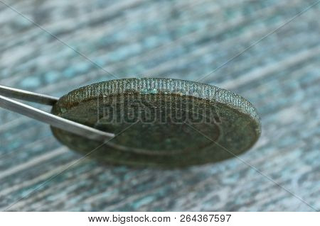 Metal Tweezers Holding Retro Copper Iron Coin On The Table