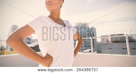 Side view of confident woman standing for breast cancer awareness against urban background