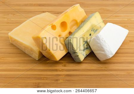 Pieces Of Blue Cheese, Brie, Medium-hard Swiss And Hard Cheese On The Bamboo Cutting Board Close-up