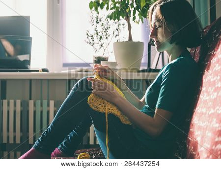 Girl Knits Crochet At Home. Woman Engaged In Needlework. A Knitter Sits On A Sofa And Works. Creativ