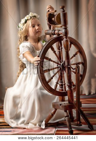 A Cute Little Girl Wove A Wool With A Rotating Wheel. Retro Style, Memories Of The Past.