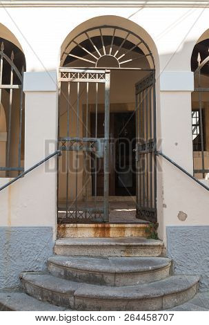 Wall Of A Building Elightened By The Sunlight With A Iron Opened Gate. Rounded Stone Stairs. Histori