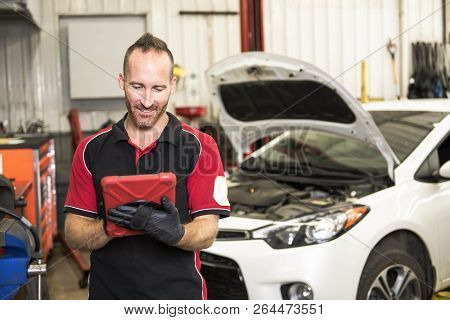 Handsome Mechanic Based On Car In Auto Repair Shop With Tablet On Hand