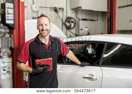 Handsome Mechanic Based On Car In Auto Repair Shop With Tablet On Hand
