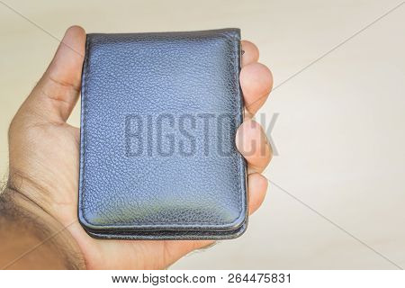 Black Wallet Closed In The Hand Of A Man. Light Background