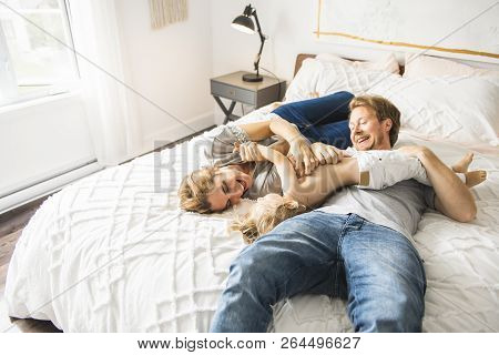 Family With Child Having Fun On Bed With Pillow Fight