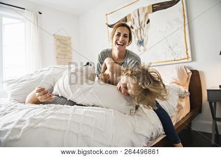 Family With Child Having Fun On Bed With Pillow Fight