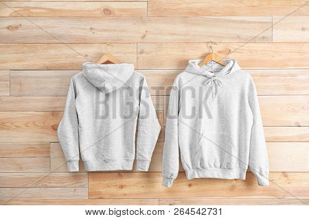 New Hoodie Sweaters With Hangers On Wooden Wall. Mockup For Design
