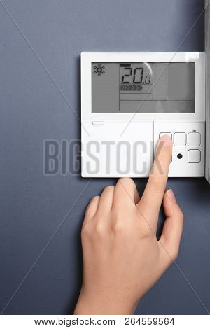 Woman Adjusting Thermostat On Grey Wall, Closeup. Heating System