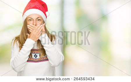 Middle age adult woman wearing winter sweater and chrismat hat over isolated background shocked covering mouth with hands for mistake. Secret concept.