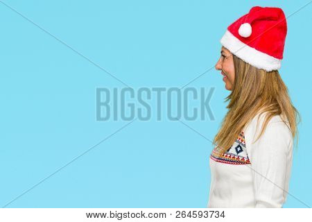 Middle age adult woman wearing winter sweater and chrismat hat over isolated background looking to side, relax profile pose with natural face with confident smile.