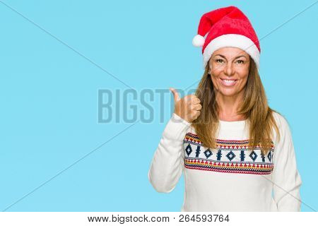Middle age adult woman wearing winter sweater and chrismat hat over isolated background doing happy thumbs up gesture with hand. Approving expression looking at the camera with showing success.