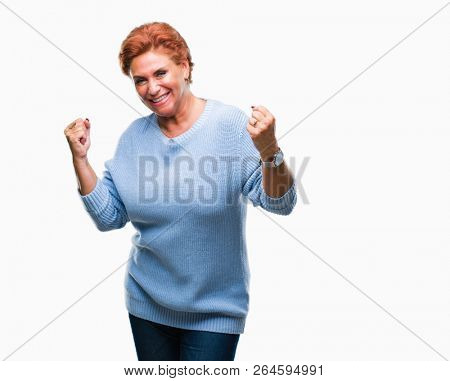 Atrractive senior caucasian redhead woman over isolated background very happy and excited doing winner gesture with arms raised, smiling and screaming for success. Celebration concept.