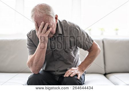 Senior Man Thinking And Sitting On Sofa At Home Like Sad