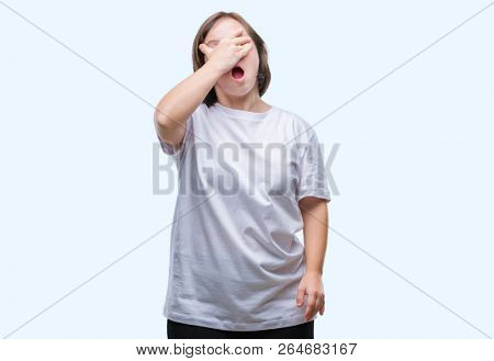 Young adult woman with down syndrome over isolated background peeking in shock covering face and eyes with hand, looking through fingers with embarrassed expression.