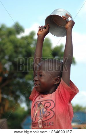 Donkorkrom, Ghana: July 20th 2016 - A Young Boy Holds A Bowl Used For Begging Above His Head Near Do