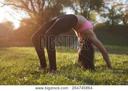 Girl Is Doing Yoga, Standing In Bridge Pose. Setu Bandhasana. With Sunset On Background.in A Park In