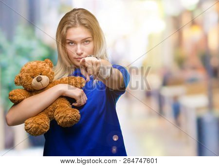 Young caucasian woman holding cute teddy bear over isolated background pointing with finger to the camera and to you, hand sign, positive and confident gesture from the front