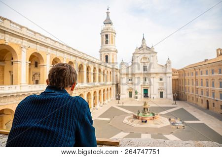 Man In Loreto With Background The Basilica In Sunny Day, Portico To The Side, People In The Square I