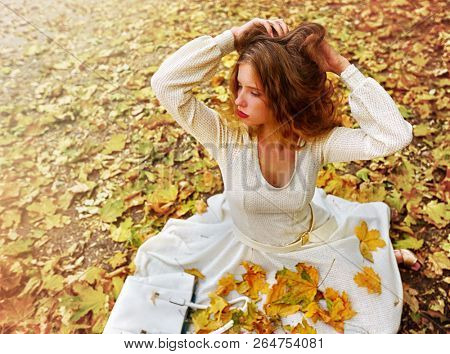 Autumn fashion feminity lace dress with long sleeve in princess style. Top view of girl model trew foliage bouquet sitting on fall leaves city park outdoor in morning sunrays.