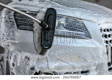 Front Light Of Silver Car Washed In Self Service Carwash. Brush Leaving Strokes In Shampoo And Foam