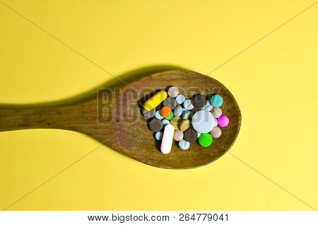 Assorted Pharmaceutical Medicine Pills, Tablets And Capsules On Wooden Spoon. Yellow Background
