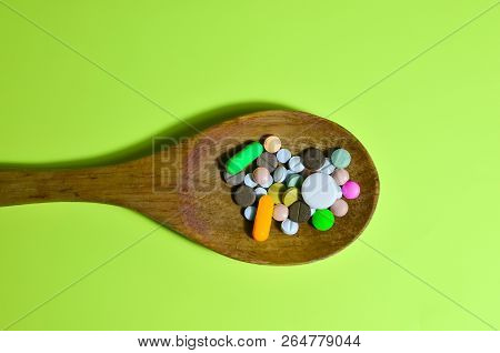Assorted Pharmaceutical Medicine Pills, Tablets And Capsules On Wooden Spoon. Green Background