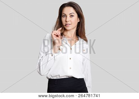 Self Confident Female Model Keeps Spectacles In Hands, Wears White Blouse And Blak Skirt, Looks With