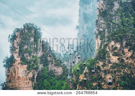 Famous tourist attraction of China - Zhangjiajie stone pillars cliff mountains in fog clouds with cable railway car lift at Wulingyuan, Hunan, China. With camera pan
