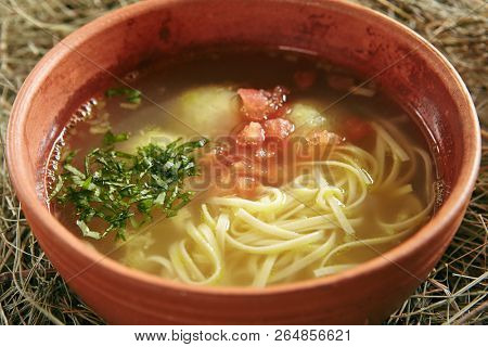 Beautiful Serving Vintage Ceramic Bowl of Homemade Noodle Soup Arishta with Chicken Meatballs. Clear Sturdy Seasoned Broth with Turkey Meat Balls, Egg Spaghetti and Greens on Rustic Background
