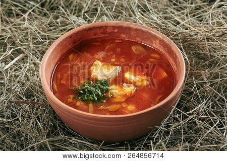 Beautiful Serving Vintage Ceramic Bowl of Red Fish Soup with Salmon and Pike Perch. Traditional Homemade Ukha, Bouillabaisse or Halaszle with Tomatoes and Vegetables on Rustic Background