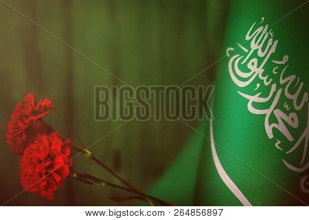 Saudi Arabia Flag With Two Red Carnation Flowers For Honour Of Veterans Day Or Memorial Day On Green
