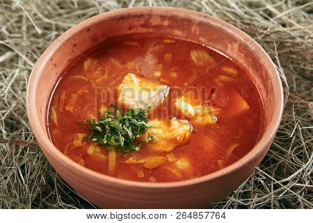 Beautiful Serving Vintage Ceramic Bowl of Red Fish Soup with Salmon and Pike Perch. Traditional Homemade Ukha, Bouillabaisse or Halaszle with Tomatoes and Vegetables on Rustic Background