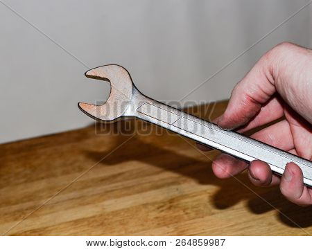 Large Metal Wrench In Man's Hand On White Wall Background. Construction Tool. Plumber