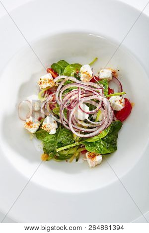 Green Salad with Goat Cheese, Spinach, Tomato and Red Onion Rings Isolated on White Background. Restaurant Starter Menu with fresh Spinacia and Chard Leaves, Tomatoes, Greens, Spices Top View