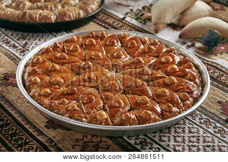 Beautiful Serving Homemade Baklava in a Round Metal Tray on Vintage Traditional Tablecloth. Sweet Turkish Style Brown Glazed Pastries Baklawa with Walnut, Nuts, Sugar, Pistachio and Honey Close Up
