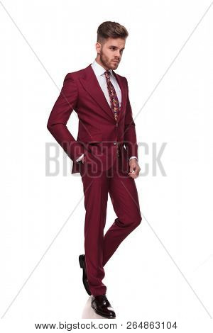 relaxed stylish man in grena suit walks on white background with a hand in pocket and looks down to side, full length picture
