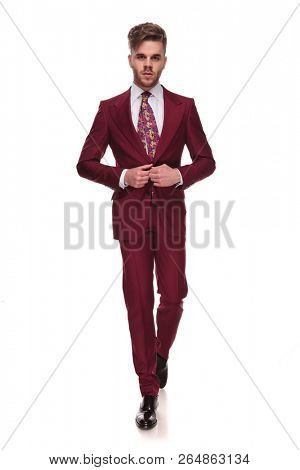 seductive elegant man stepping forward on white background and buttoning grena suit, full length picture