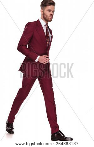 young gentleman in grena suit steps to side on white background while looking down, full body picture