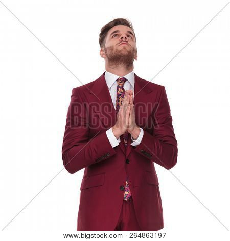 young businessman in grena suit praying and looking up while standing on white background, portrait picture
