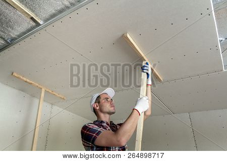 Young Worker In Protection Work Gloves Fixing Wooden Holders For Drywall Suspended Ceiling To Metal 