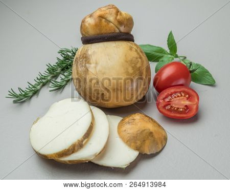 Traditional Italian smoked Scamorza cheese with herbs and tomatoes on gray background.