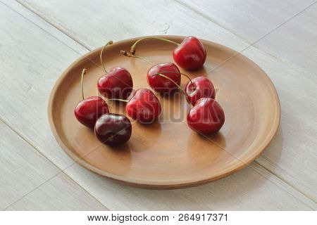 Ripe Red Tasty Sweet Cherry On A Round Ceramic Dish Handmade. Light Wooden Background